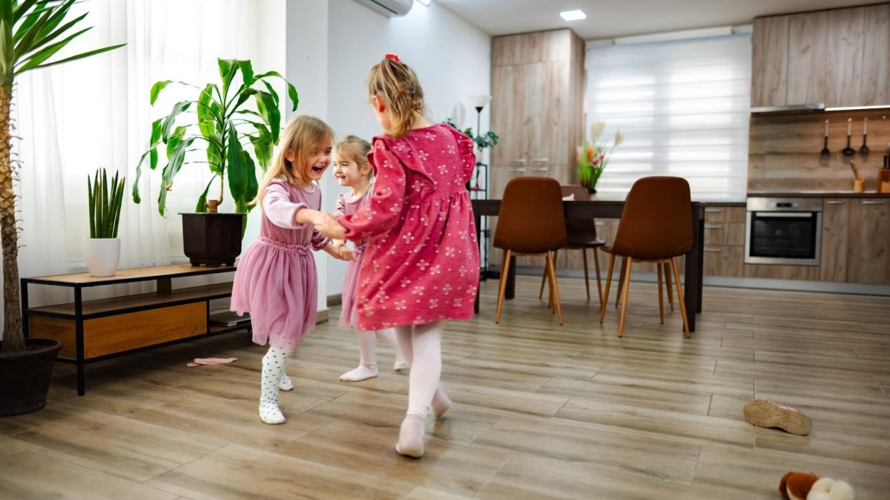 Three happy girls playing and dancing on vinyl flooring in a sunlit, contemporary living space