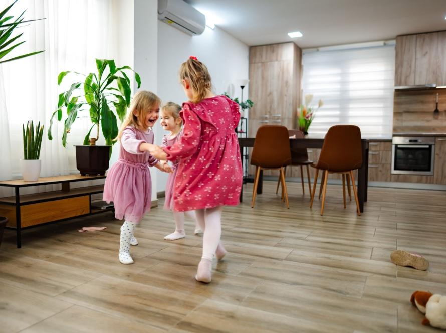 Three happy girls playing and dancing on vinyl flooring in a sunlit, contemporary living space