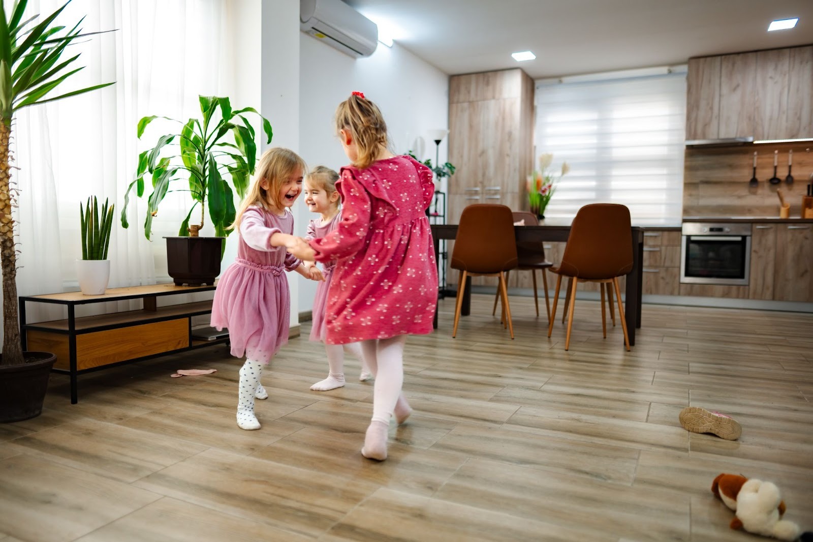 Three happy girls playing and dancing on vinyl flooring in a sunlit, contemporary living space