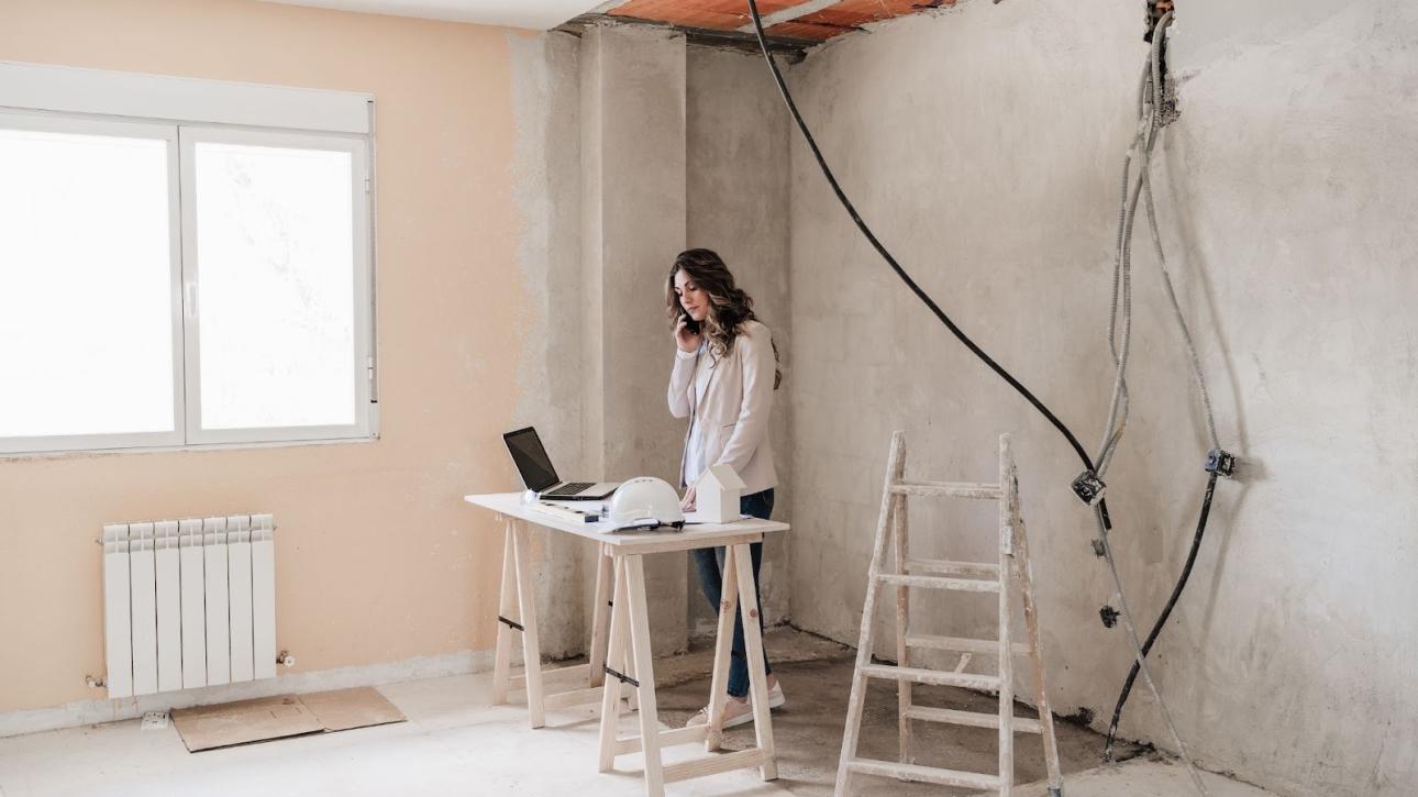 A female architect on a call at the site discussing renovation project issues while checking the blueprints