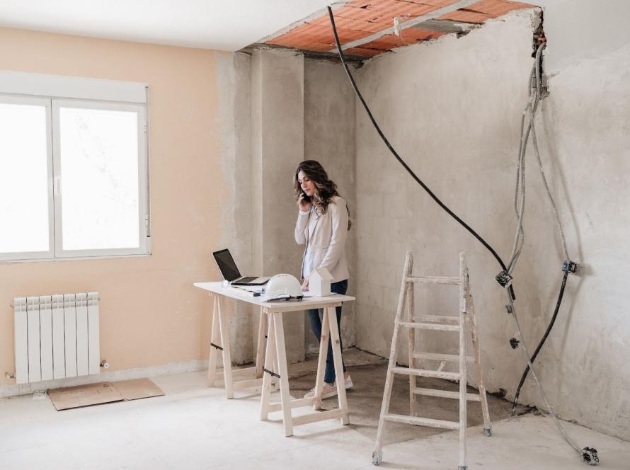 A female architect on a call at the site discussing renovation project issues while checking the blueprints