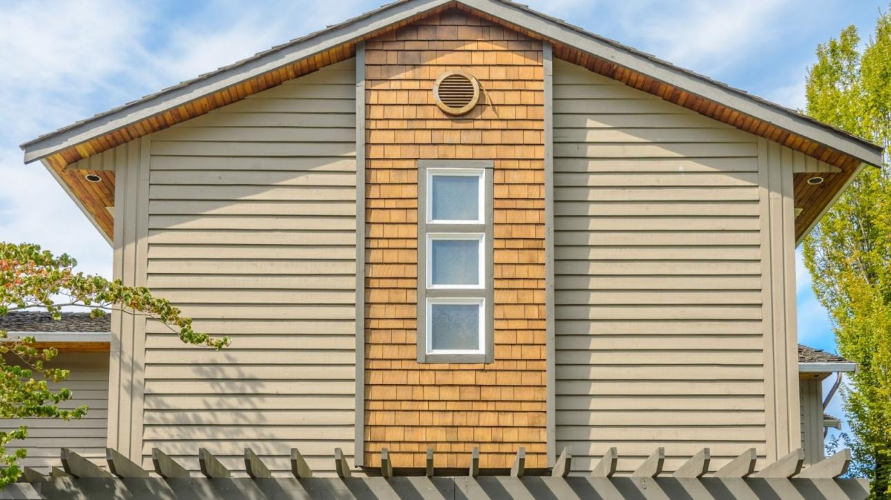 Upper exterior of a home featuring beige vinyl siding and clean white-framed windows