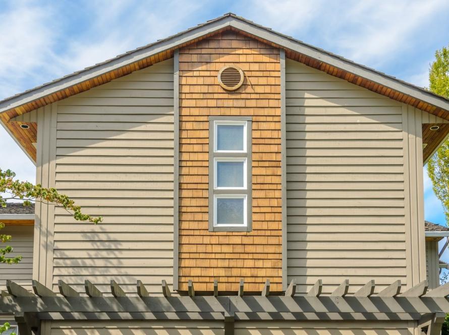 Upper exterior of a home featuring beige vinyl siding and clean white-framed windows